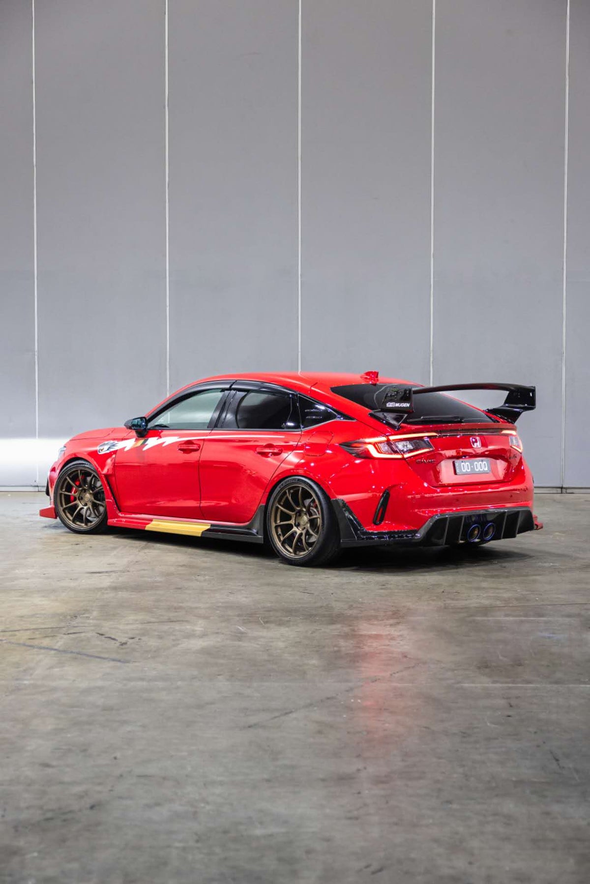 Rear three quarter view of a red FL5 Civic Type R with side graphic decal and Mugen rear wing