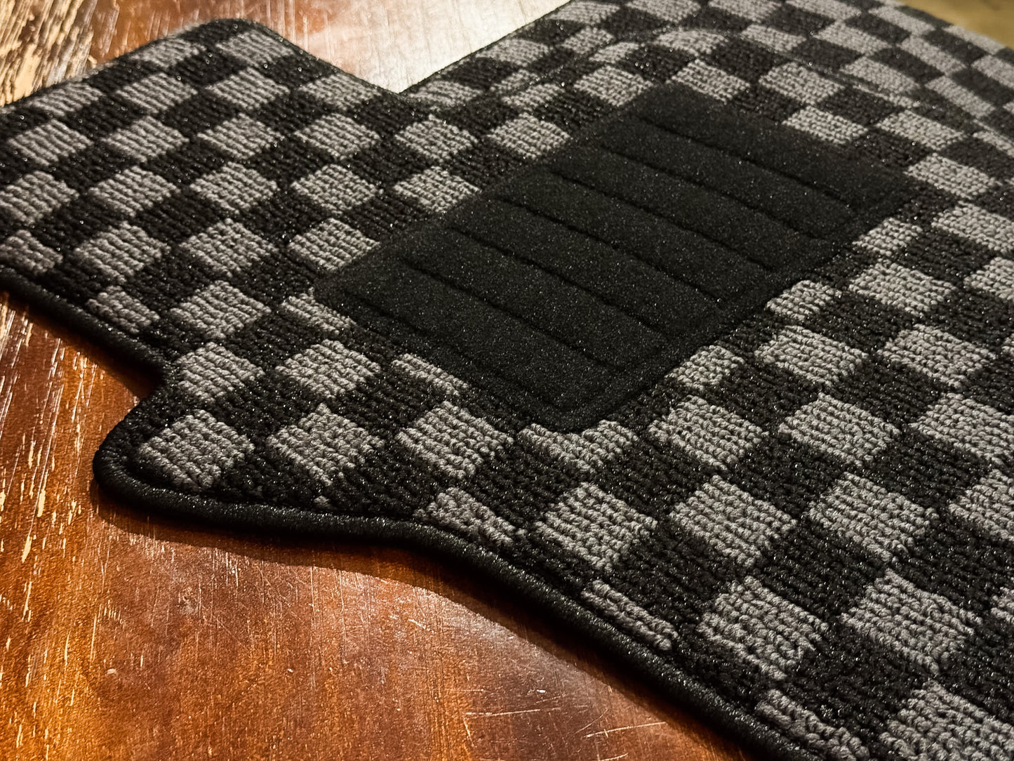 Driver mat showing the ribbed black nylon heel pad over checker carpet