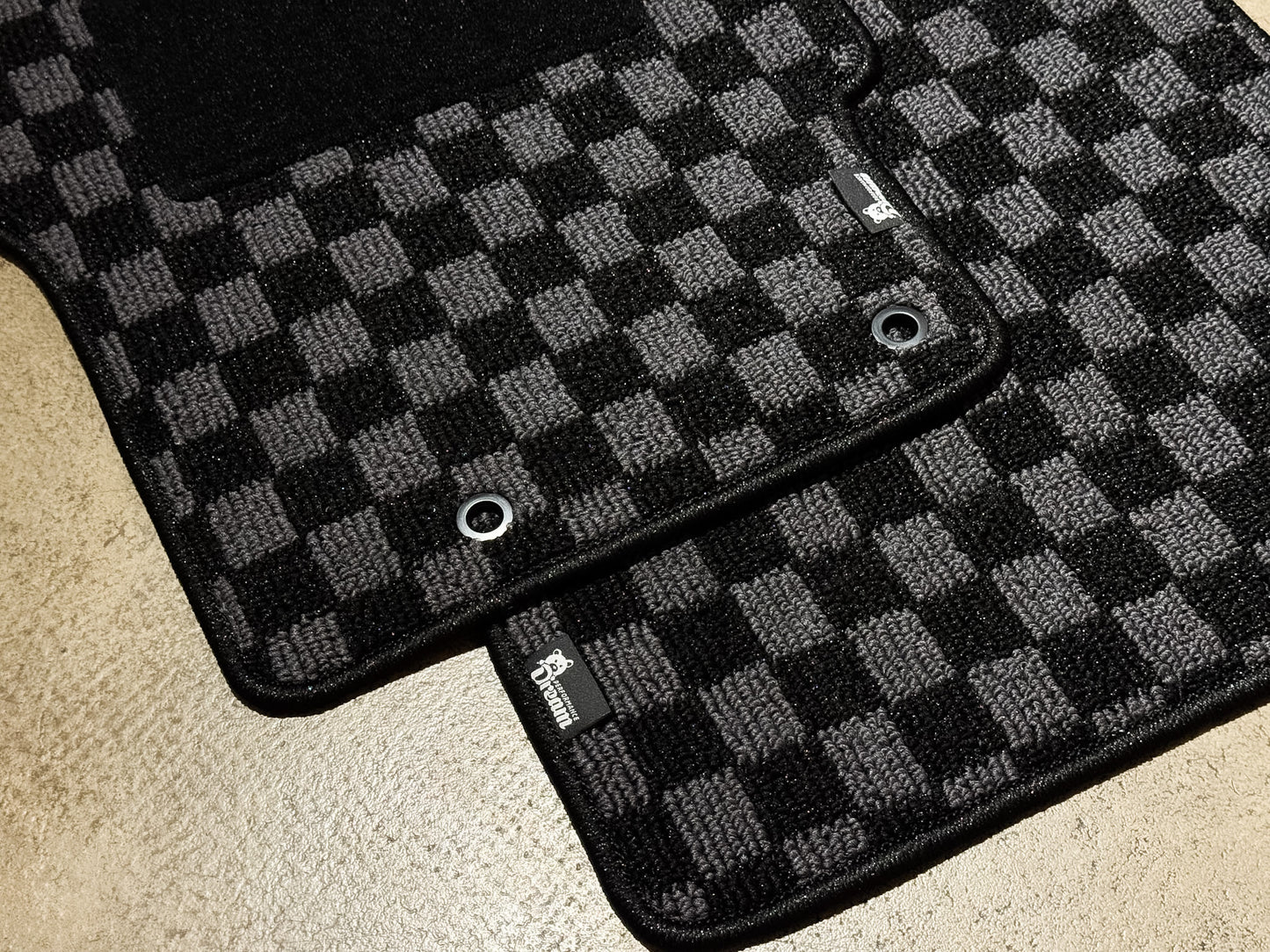 Two checker floor mats overlapping, showing the chrome fixing eyelets