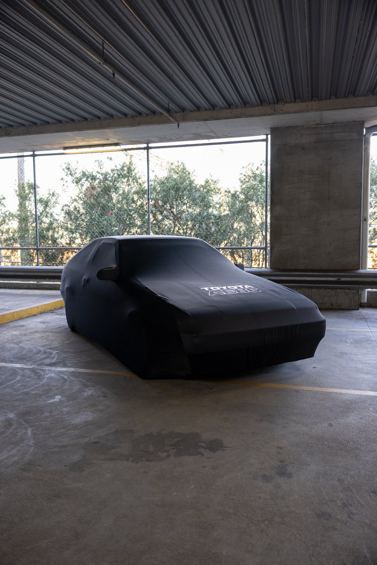Fully covered Toyota AE86 in a car park, front three quarter view